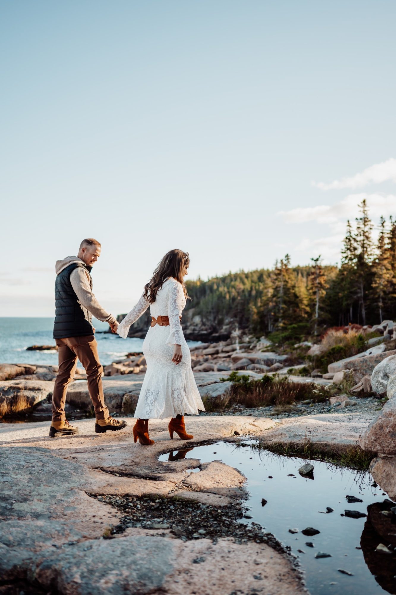 Couple holding hands on rocky Acadia shoreline during fall elopement in Maine