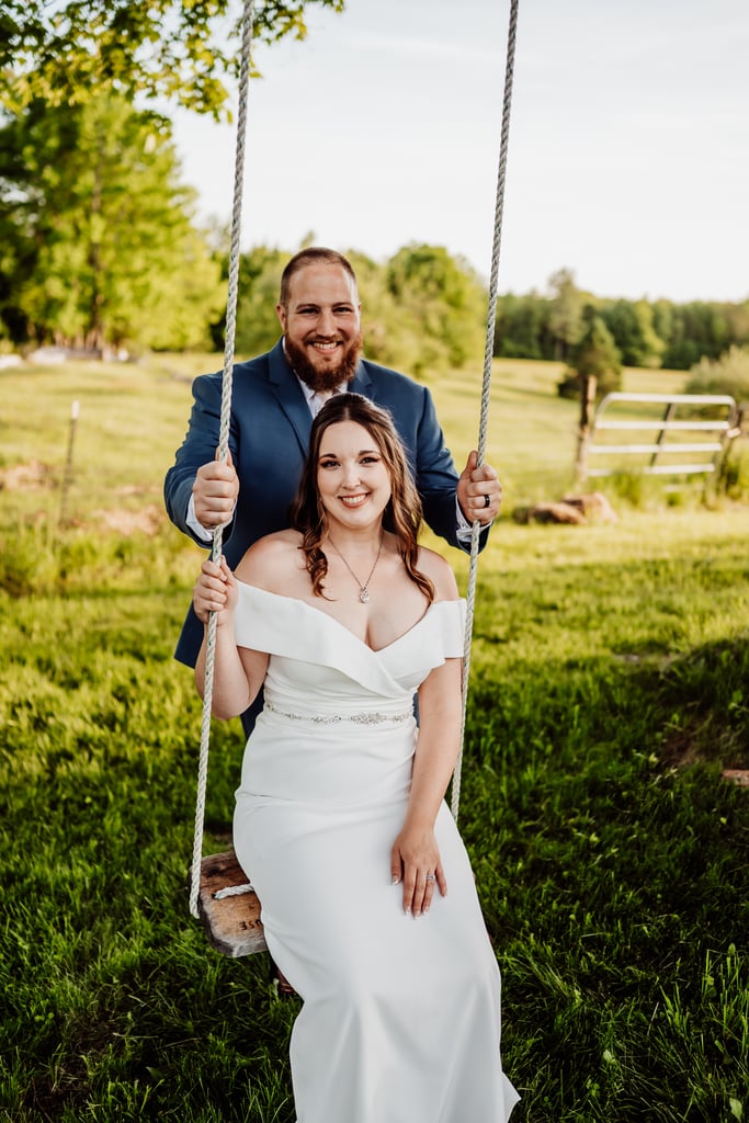 Groom standing behind bride on a swing, both smiling.