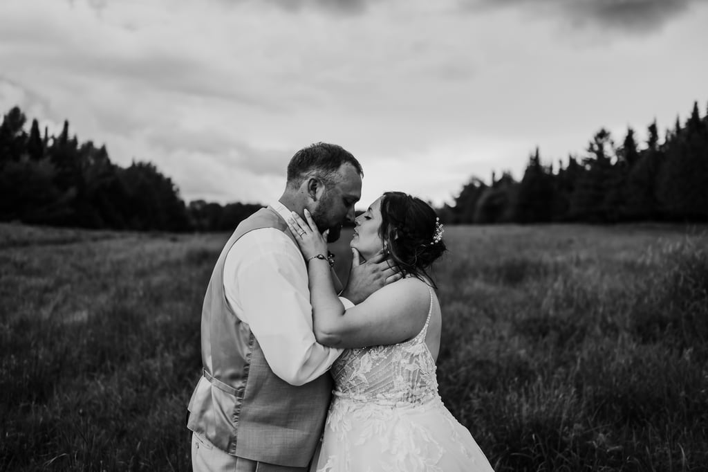 black and white photo of a bride and groom standing in a field holding each others faces