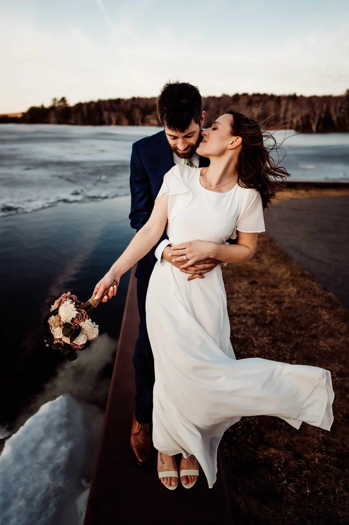 Bride and groom in front of a partially frozen lake in Greenville Maine