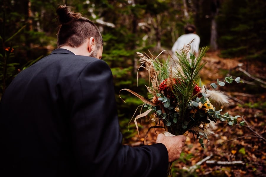 groom holding brides flowers walking through the woods