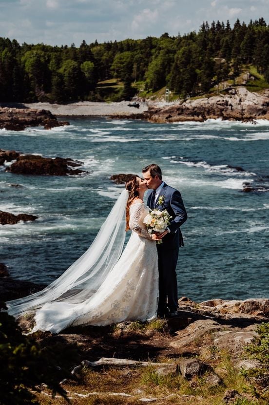 Bride and groom standing together in front of whitecaps on the ocean coast