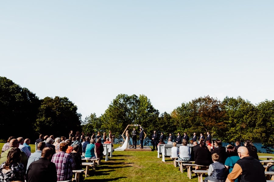 full wedding party with audience during ceremony at waters edge estate