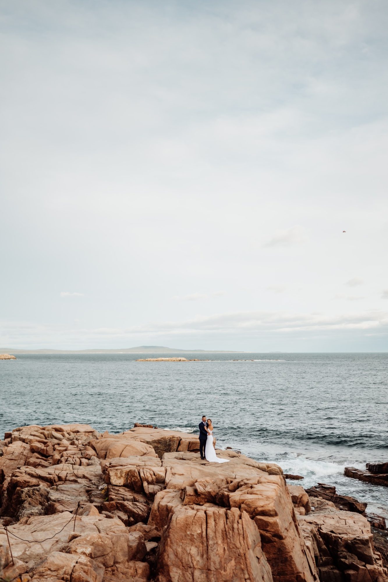 Bride and groom standing on granite cliffs next to the ocean