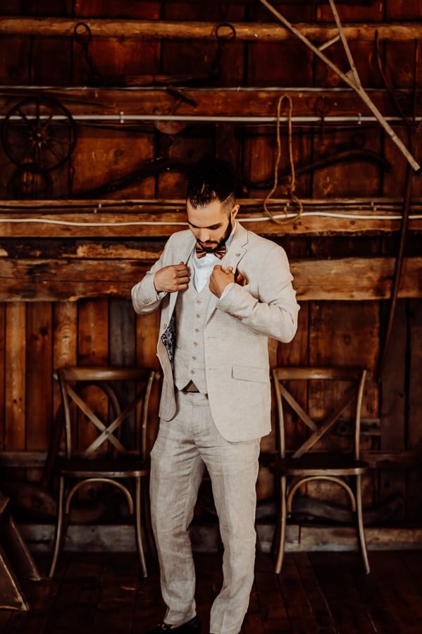 Groom adjusting tie against barn wall at clarks cove farm inn