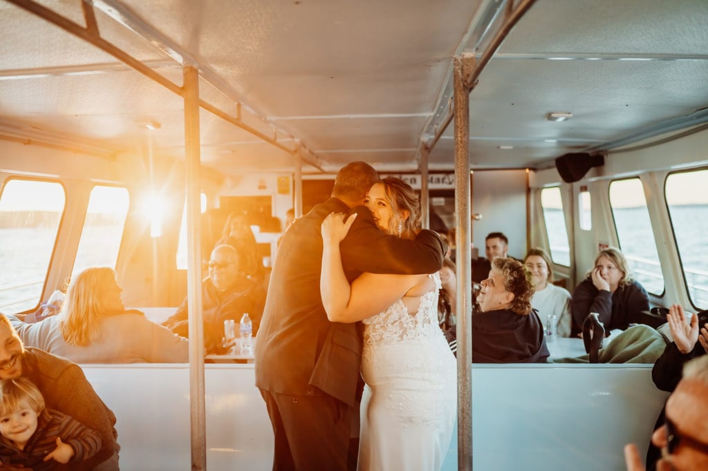 Bride and groom hugging during their first dance at sunset on their Bar Harbor wedding cruise, guests smiling and clapping in the background.
