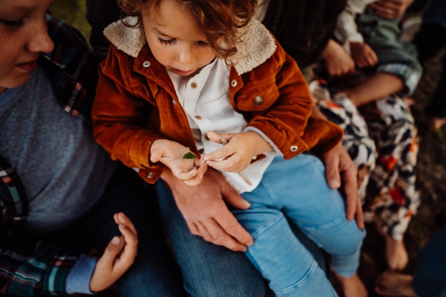 Little boy wearing orange corduroy jacket holding seaglass on dads lap