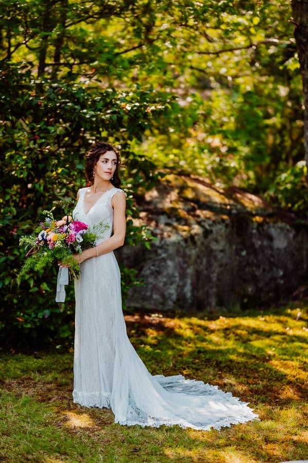 Bride holding flowers and looking over shoulder in front of trees
