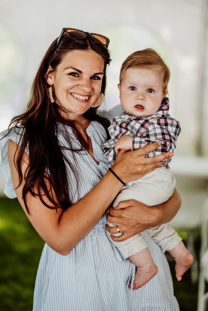 A woman smiling and holding a baby, both dressed in casual, summer attire at a wedding reception.