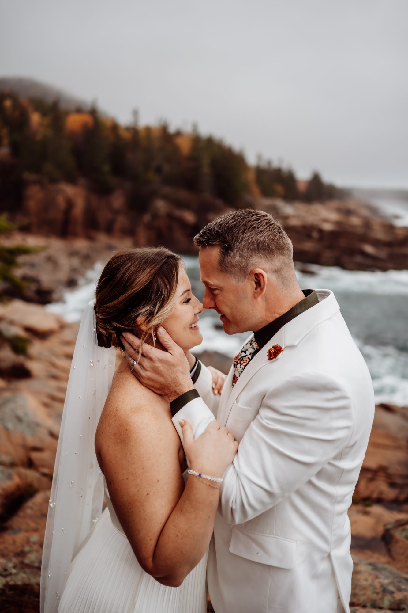 Bride and groom touching foreheads with ocean cliffs behind them at Thunder Hole in Acadia.