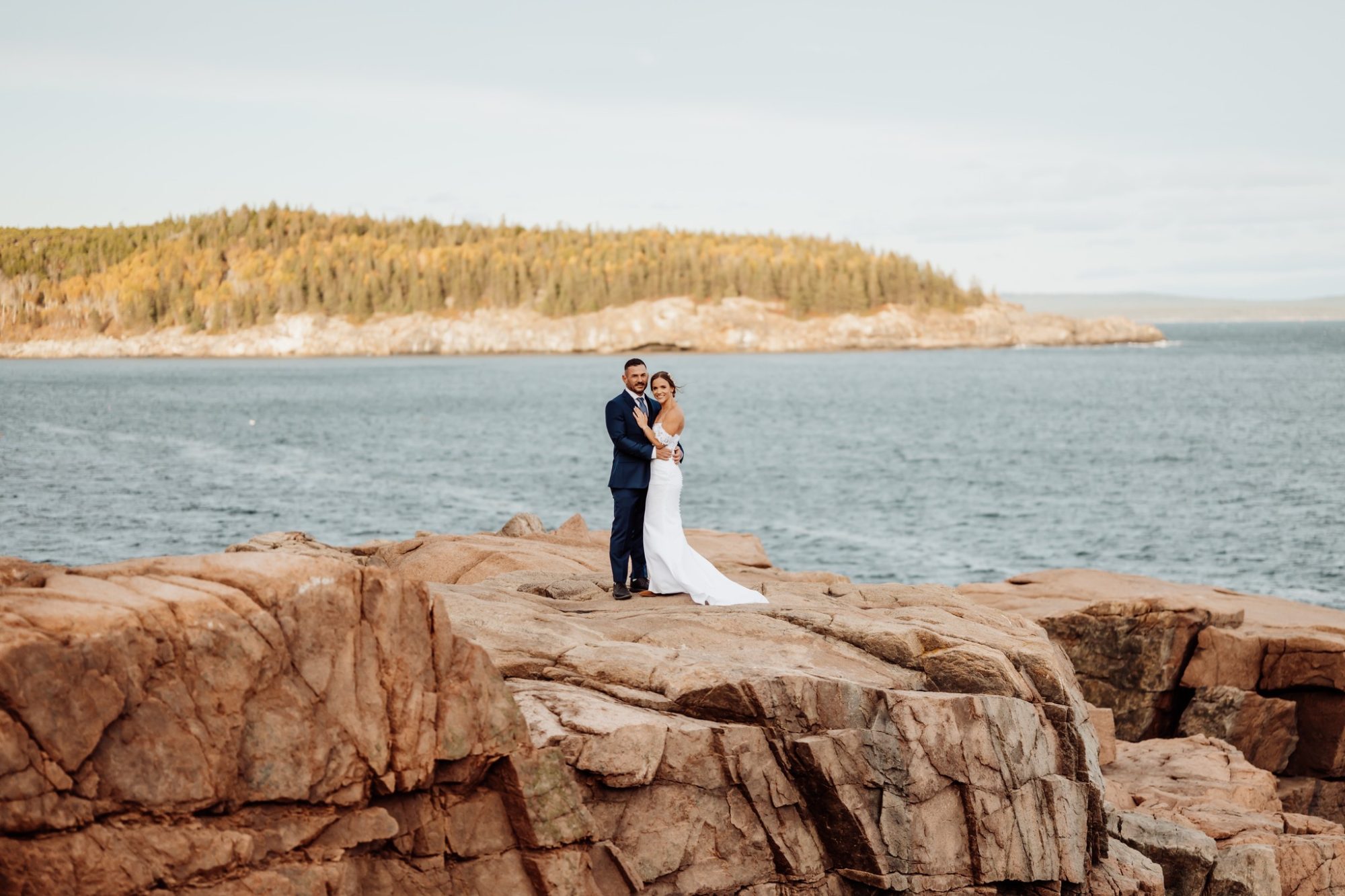 Bride and groom standing together on granite cliffs at Schooner Head Overlook in Acadia National Park overlooking the Atlantic Ocean.