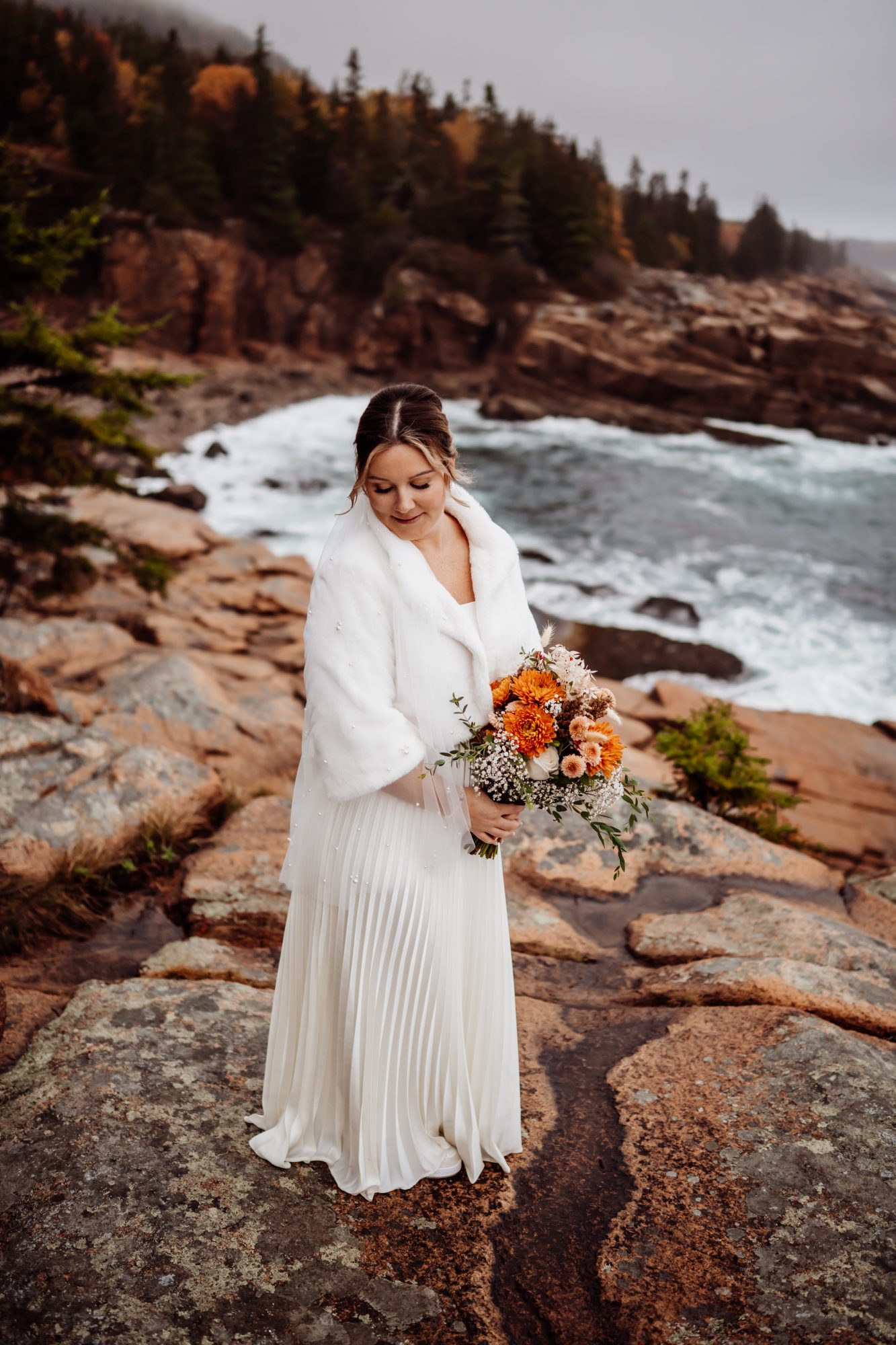 Bride standing on coastal cliffs with bouquet at Thunder Hole in Acadia.