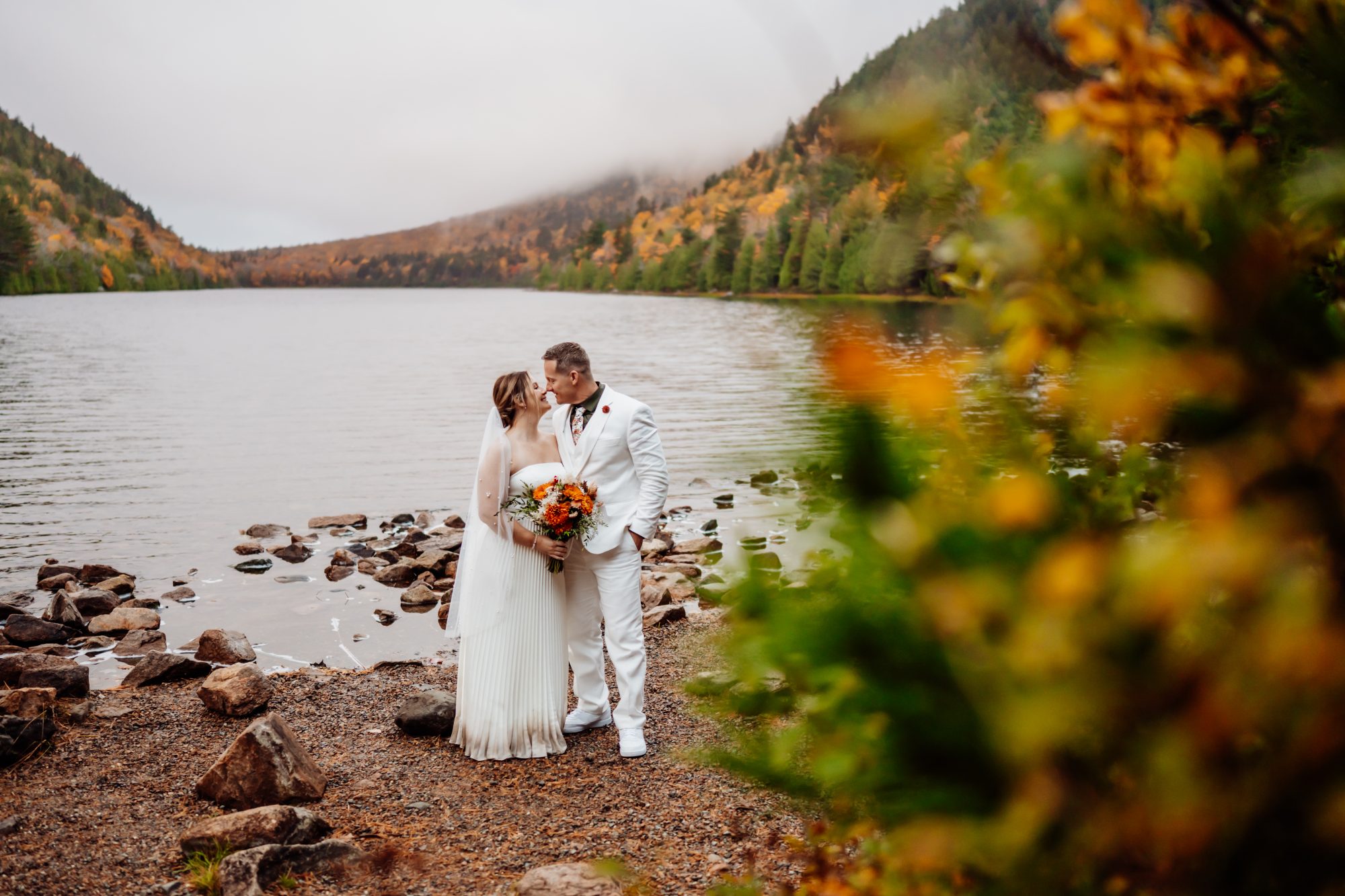 Couple embracing beside Jordan Pond during autumn elopement in Acadia National Park.
