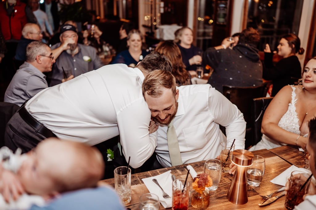 Groom laughing and hugging a friend during wedding toasts at their intimate Bar Harbor reception.