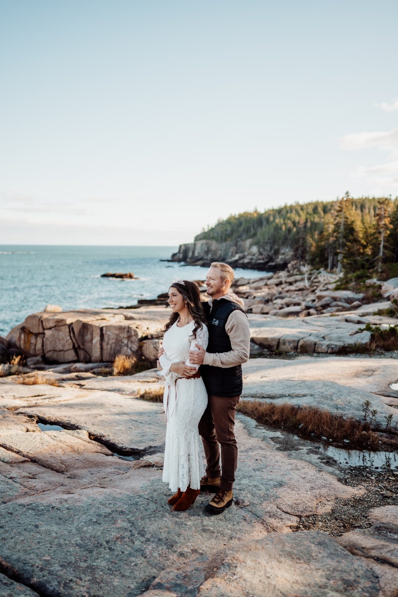 Couple standing on granite shoreline overlooking the Atlantic in Acadia during fall.