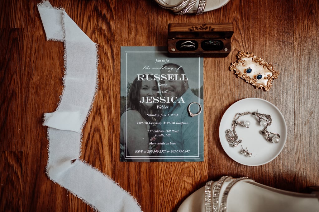 A flat lay of wedding details including an invitation, jewelry, shoes, and accessories arranged on a wooden surface
