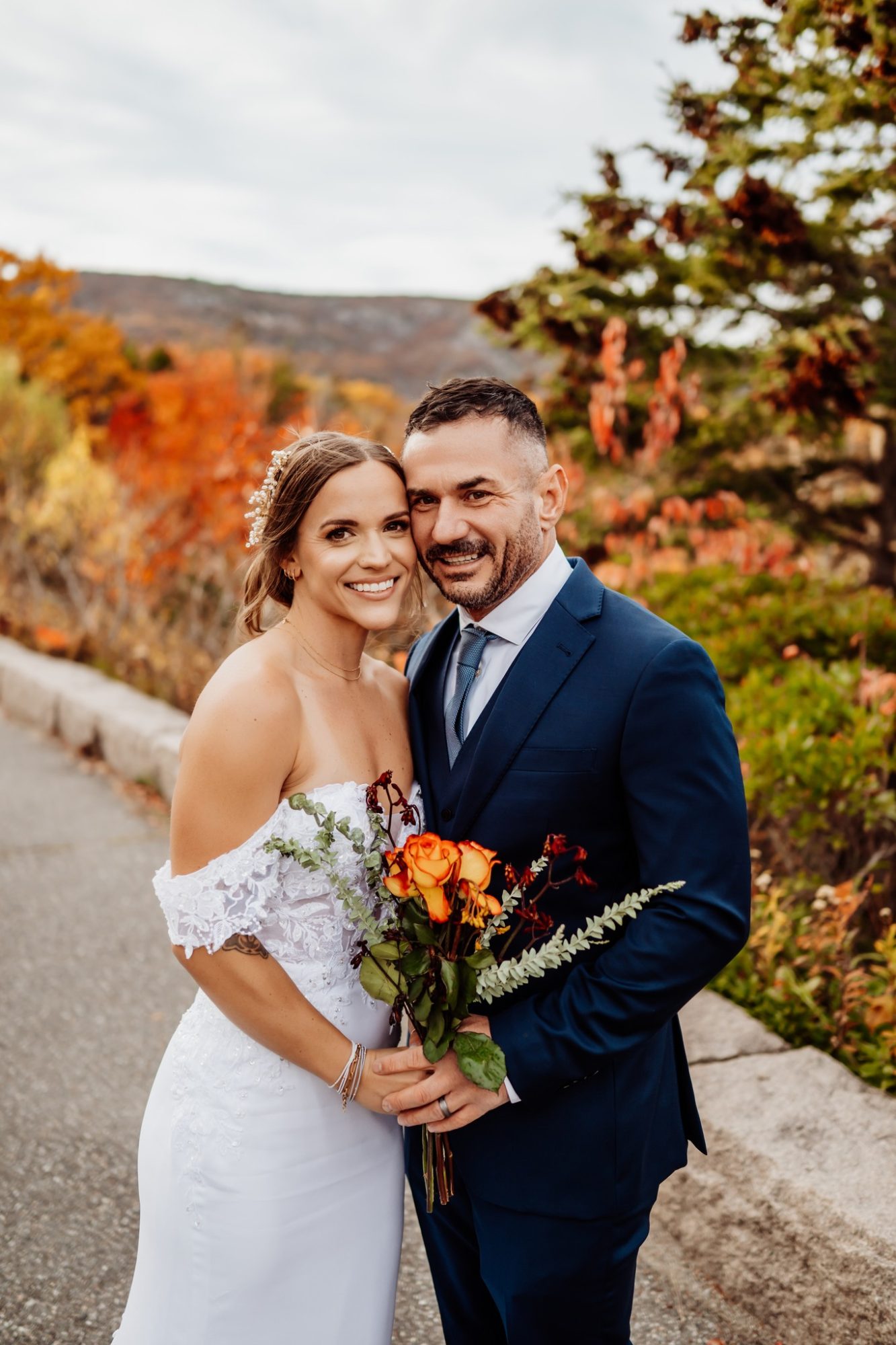 Newly married couple smiling with fall foliage behind them after their Schooner Head Overlook elopement in Acadia National Park.