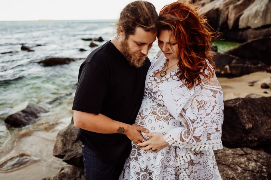 man and woman close together holding pregnant stomach in ocean