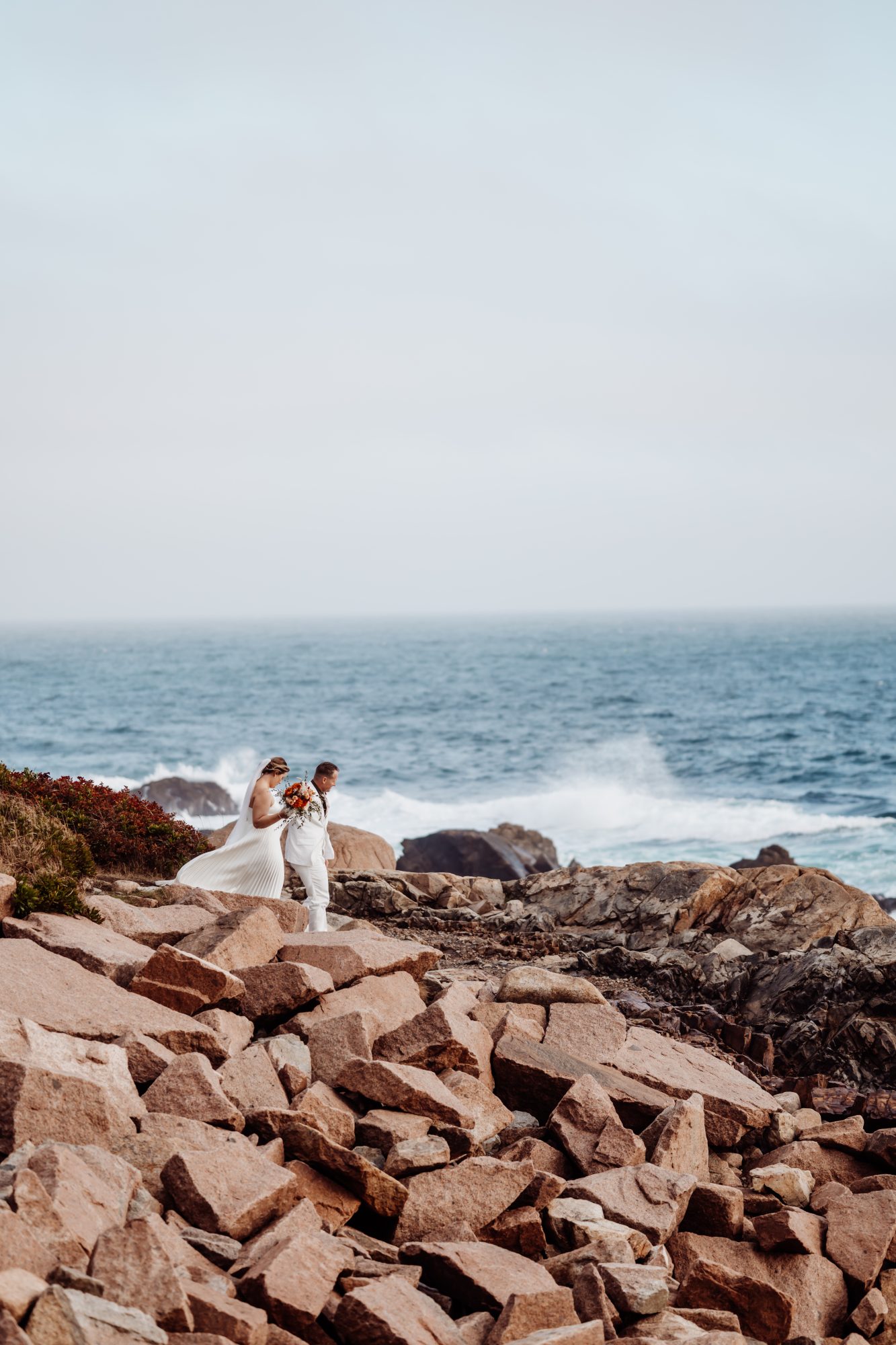 Couple embracing on rocky shoreline as waves crash at Thunder Hole in Acadia.