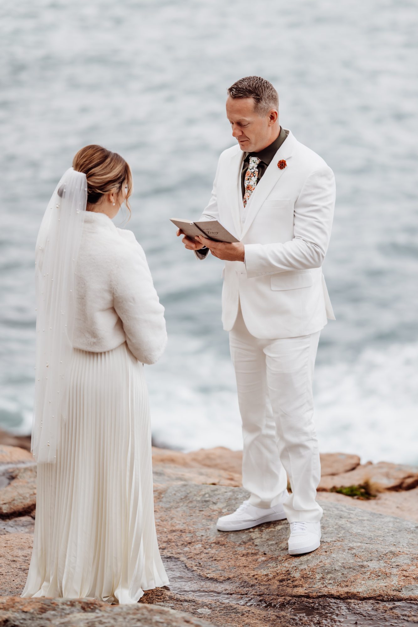 Bride and groom exchanging vows on rocky coastline at Thunder Hole in Acadia National Park.
