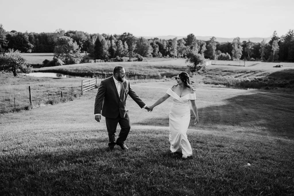 The bride and groom walk hand in hand in a field, black and white photo.