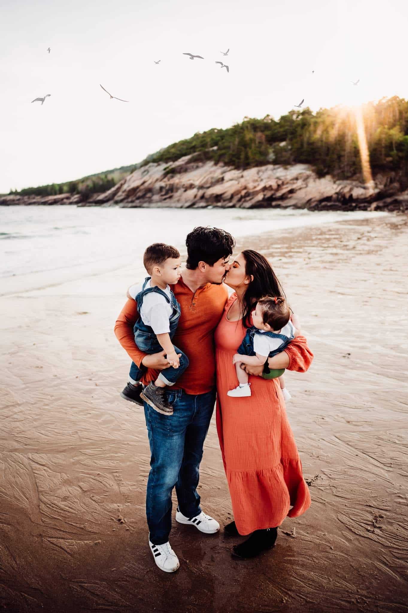 Family of four standing on sand beach at sunset