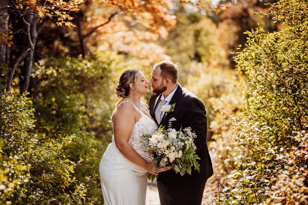 Bride and groom sharing a romantic kiss surrounded by golden autumn foliage during their Acadia National Park elopement.
