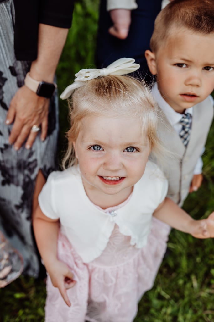 A young girl with bright eyes and a bow in her hair smiling up at the camera, with a young boy standing beside her.