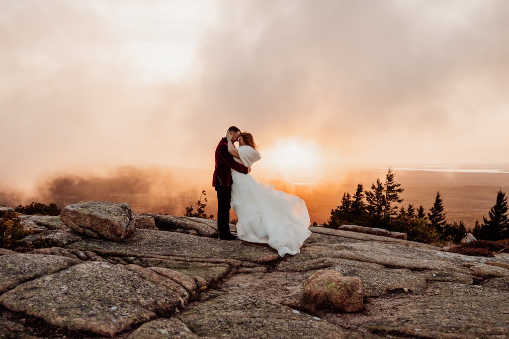 Bride and groom embracing each other as clouds move behind them on top of the mountain