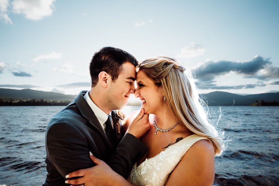 Bride and groom touching foreheads at sunset on lake