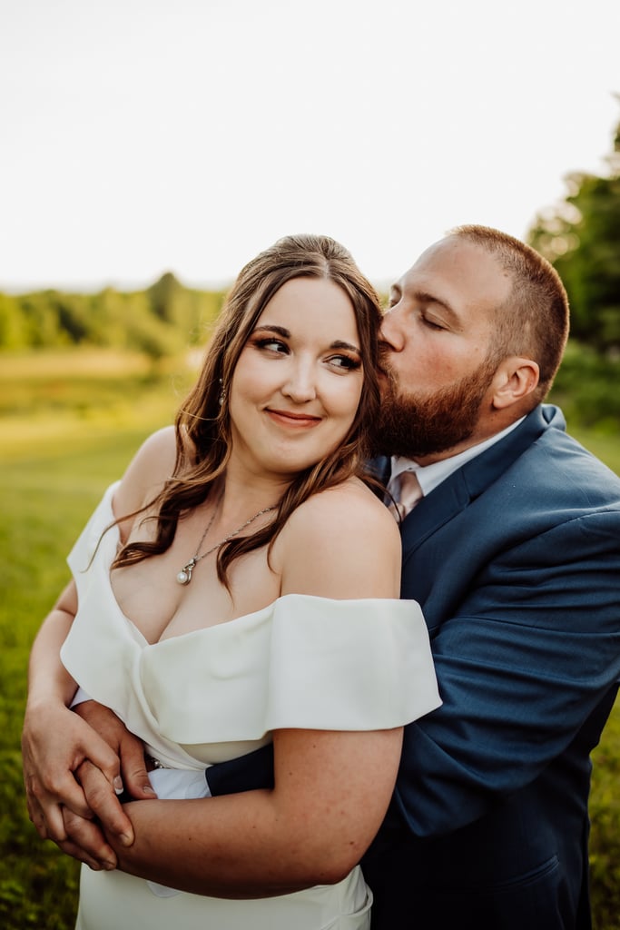 A man in a blue suit kissing his bride who is wearing a white off-shoulder dress