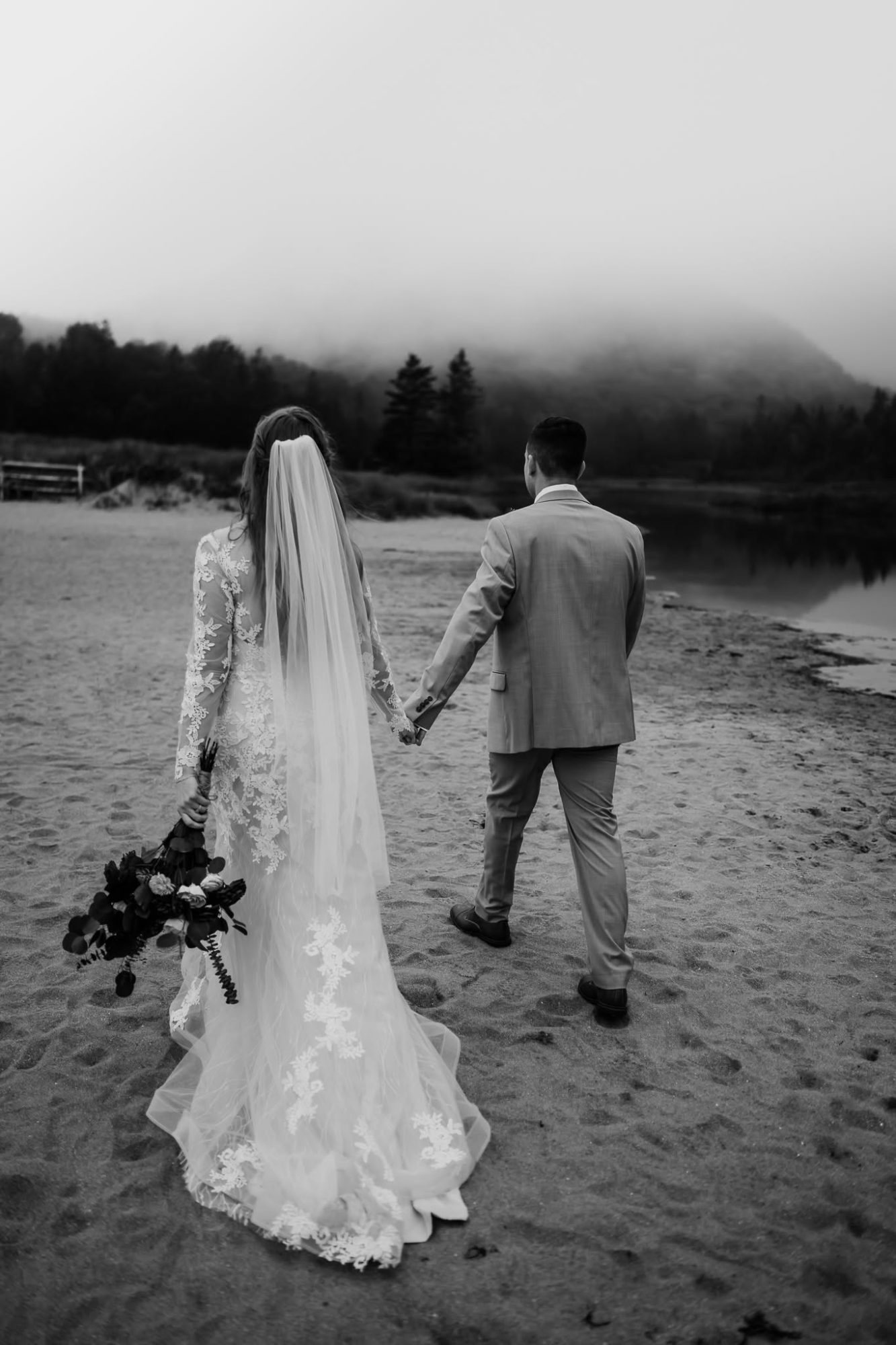 Bride and groom walking away in the fog on sand beach