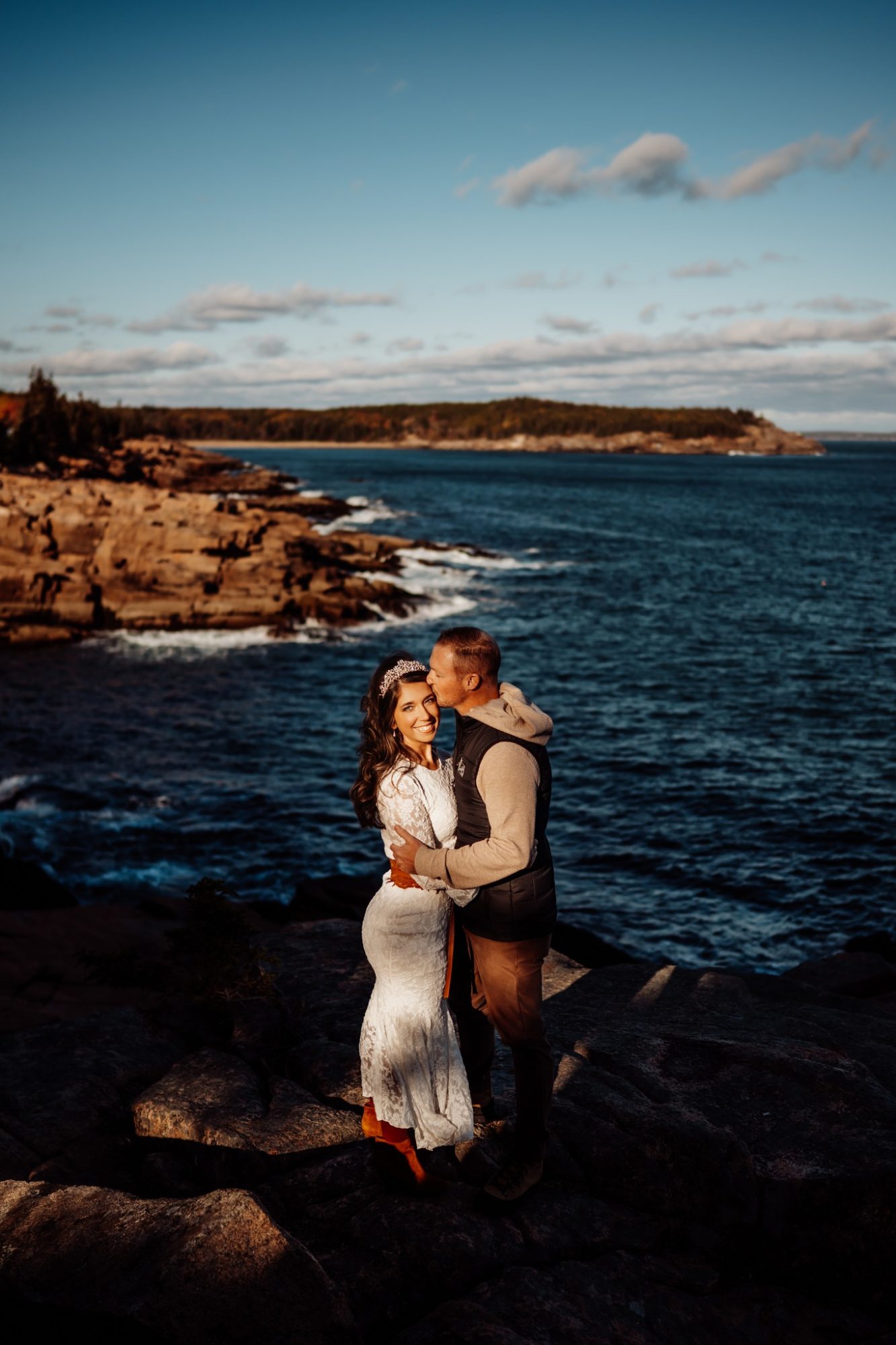 couple embracing at sunset on Acadia’s rocky coastline during autumn elopement.