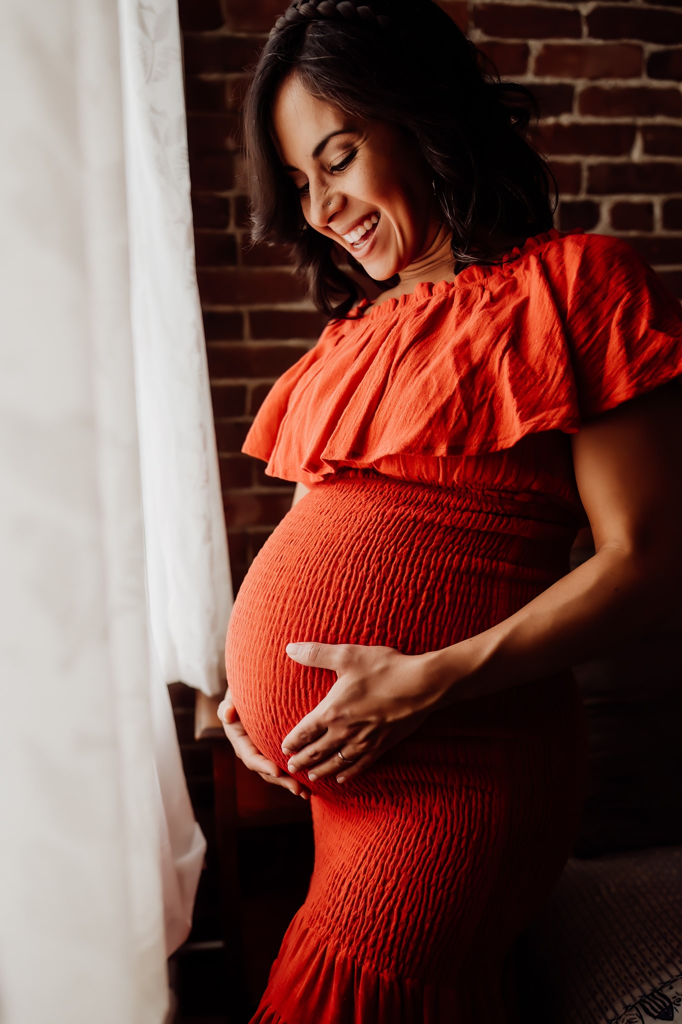 Woman smiling at her pregnant belly wearing a festive red dress