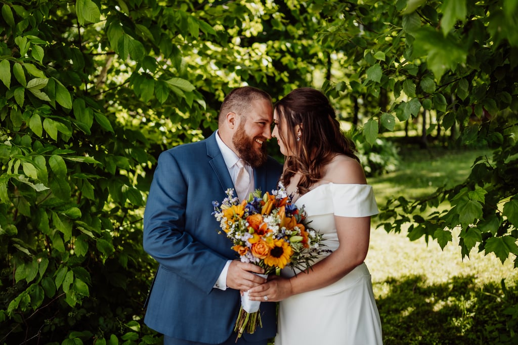 A bride and groom standing close together, smiling, with the bride holding a colorful bouquet of flowers.