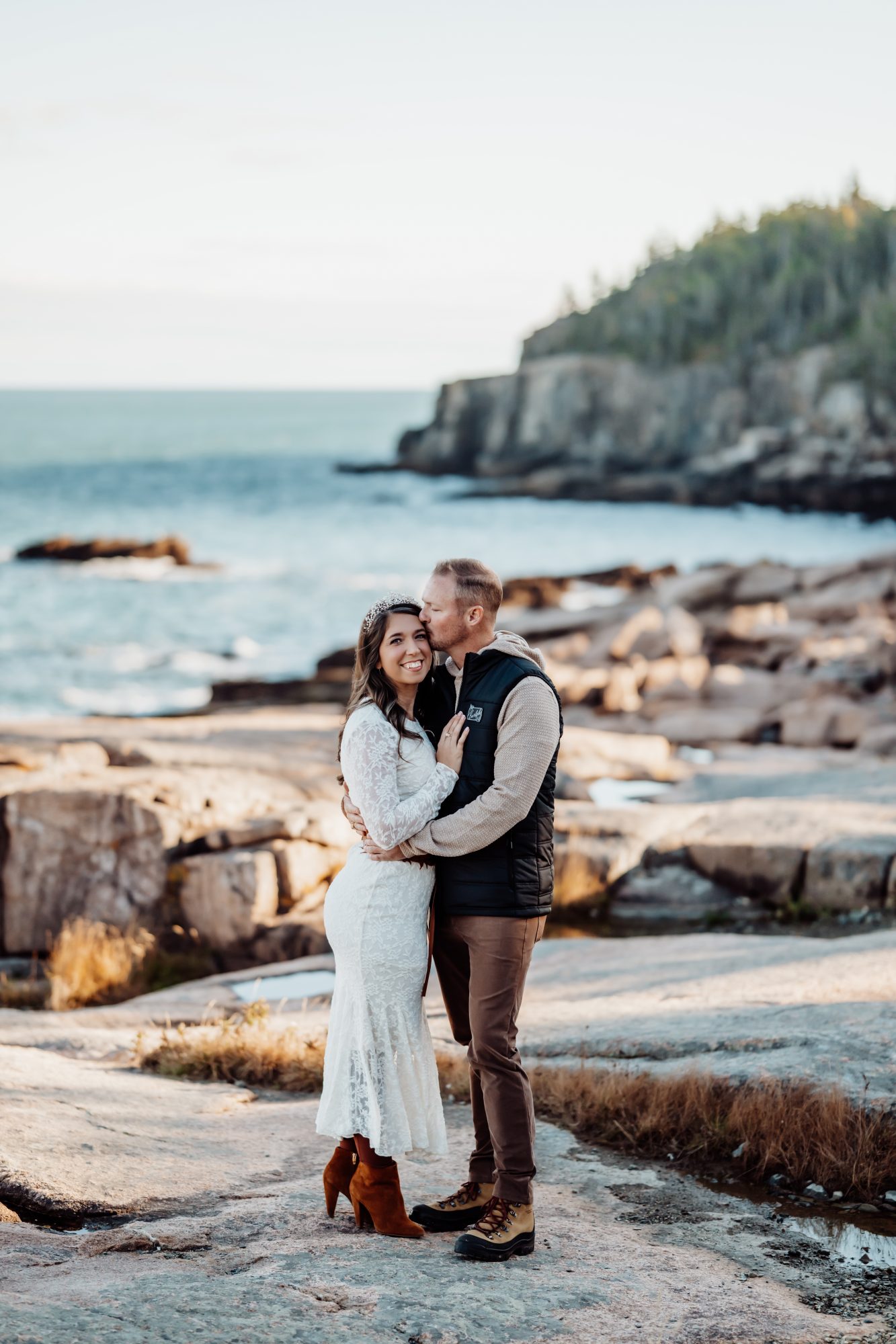 Newlyweds smiling together on granite shoreline overlooking the Atlantic in Acadia.