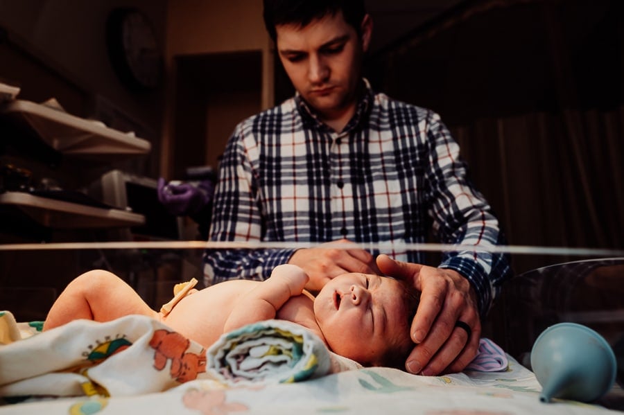 Father standing above newborn baby laying in warmer