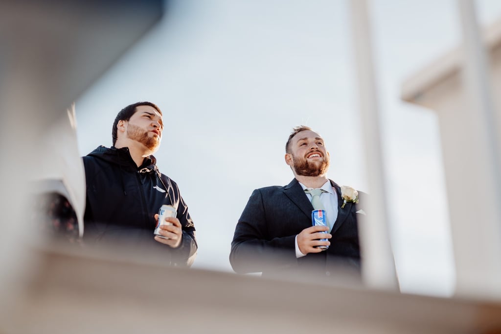 Candid moment of the groom and a guest laughing together on the upper deck of the boat, enjoying drinks during the Maine coast wedding cruise.