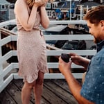 Woman holding hands over her face as she is proposed to on bridge