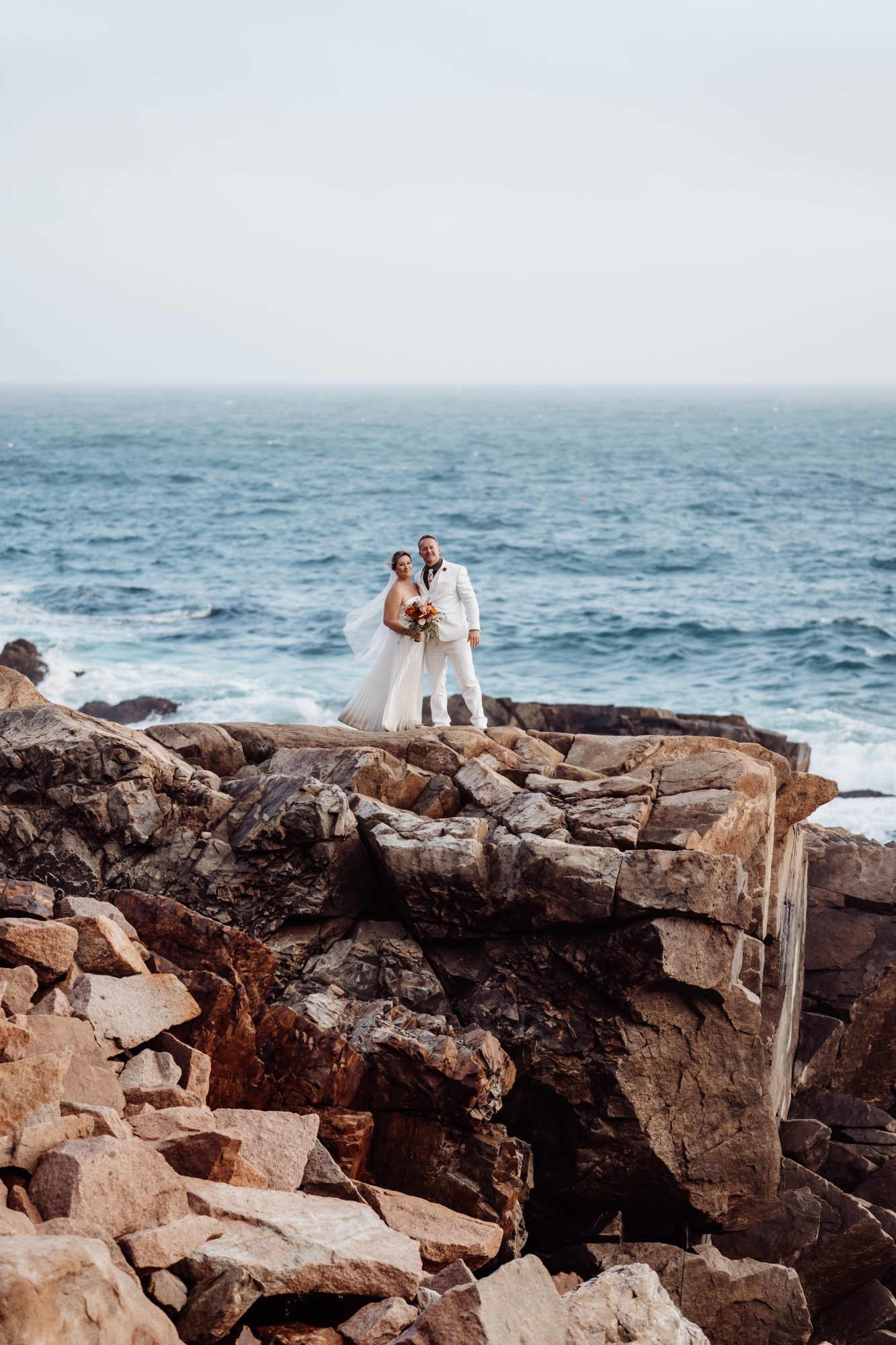 ride and groom standing on granite cliffs during Thunder Hole elopement in Acadia National Park.
