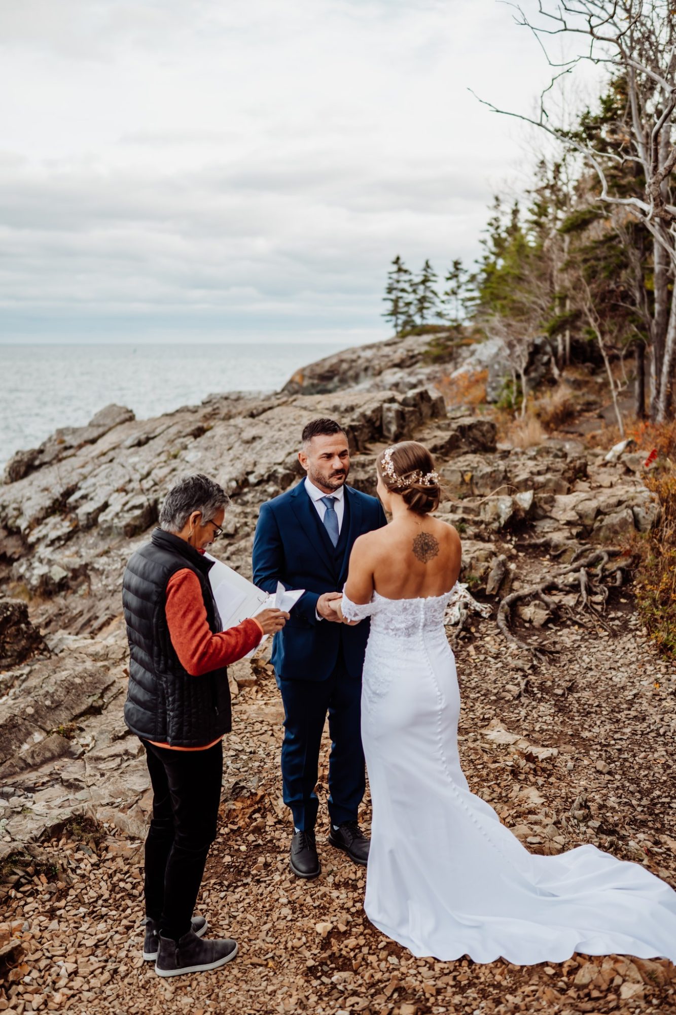 Bride and groom holding hands during a coastal elopement ceremony at Schooner Head Overlook in Acadia National Park.