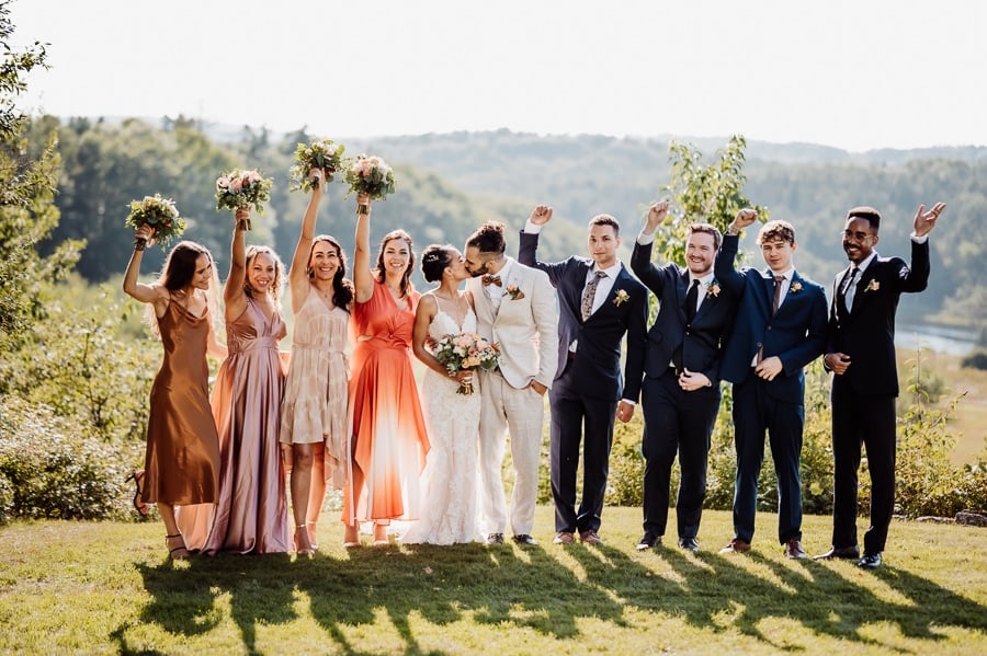 Bridal party celebrating with arms up as couple kiss