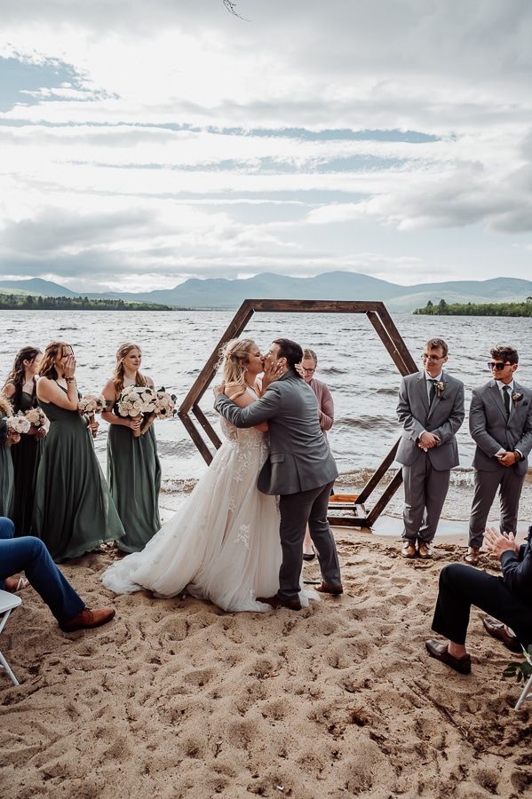 Bride and groom first kiss in front of octagon wedding arbor and lake