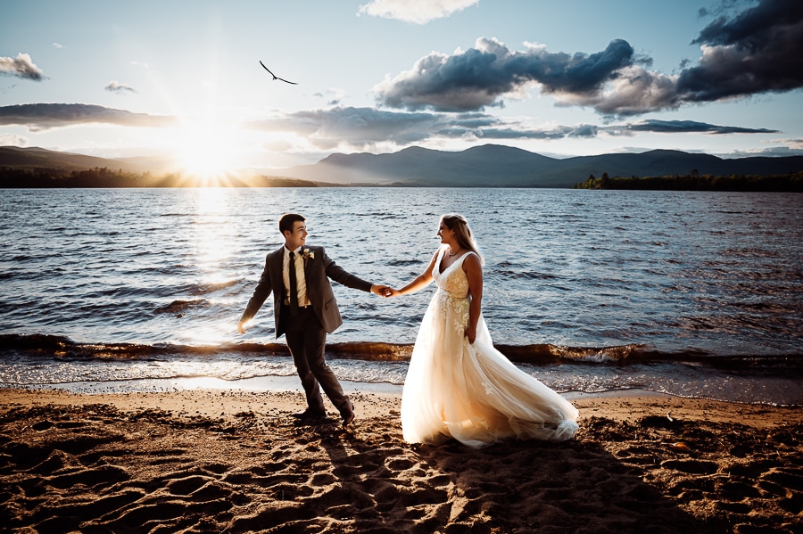 Bride and groom walking on beach at sunset