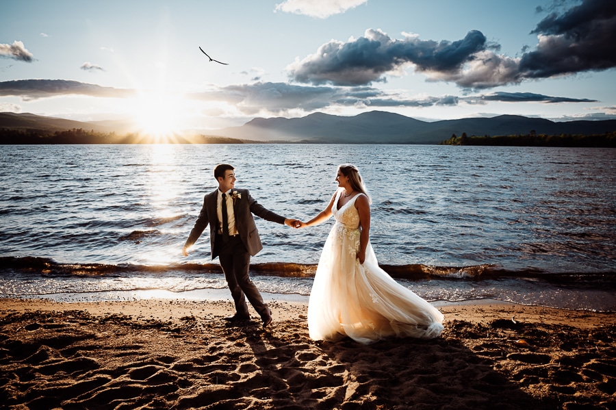 Bride and groom walking on beach at sunset