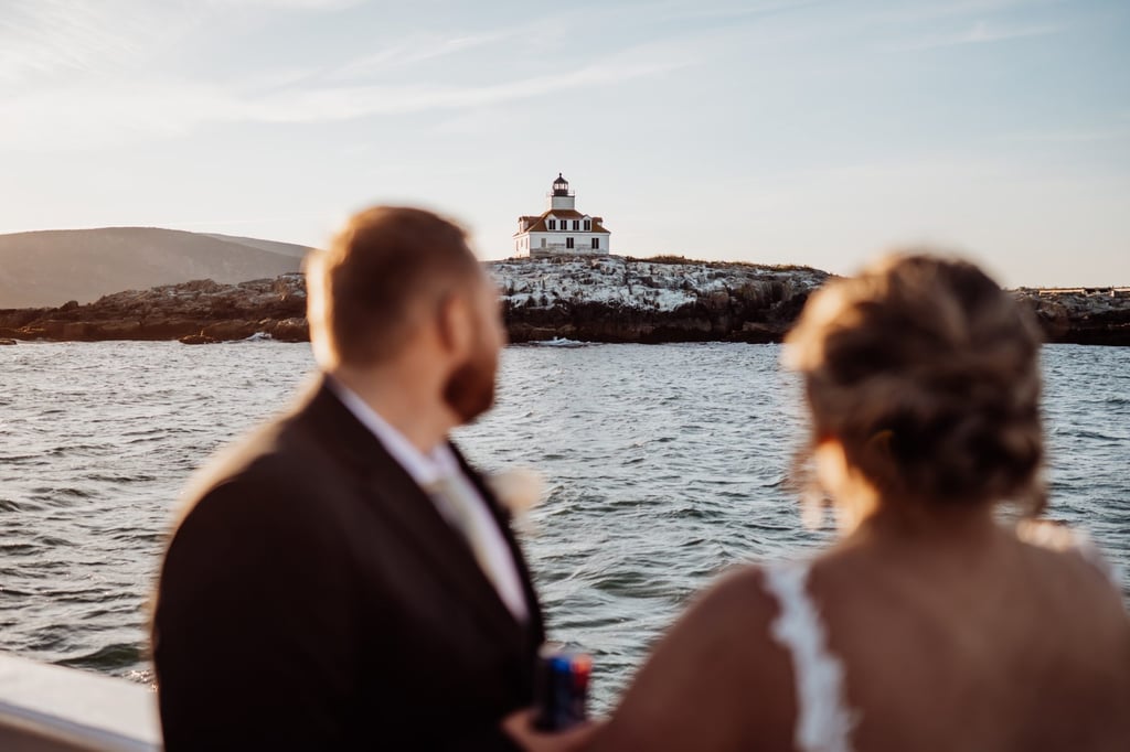 Bride and groom gazing out at the Bass Harbor Head Lighthouse from their wedding cruise boat as the sun begins to set.