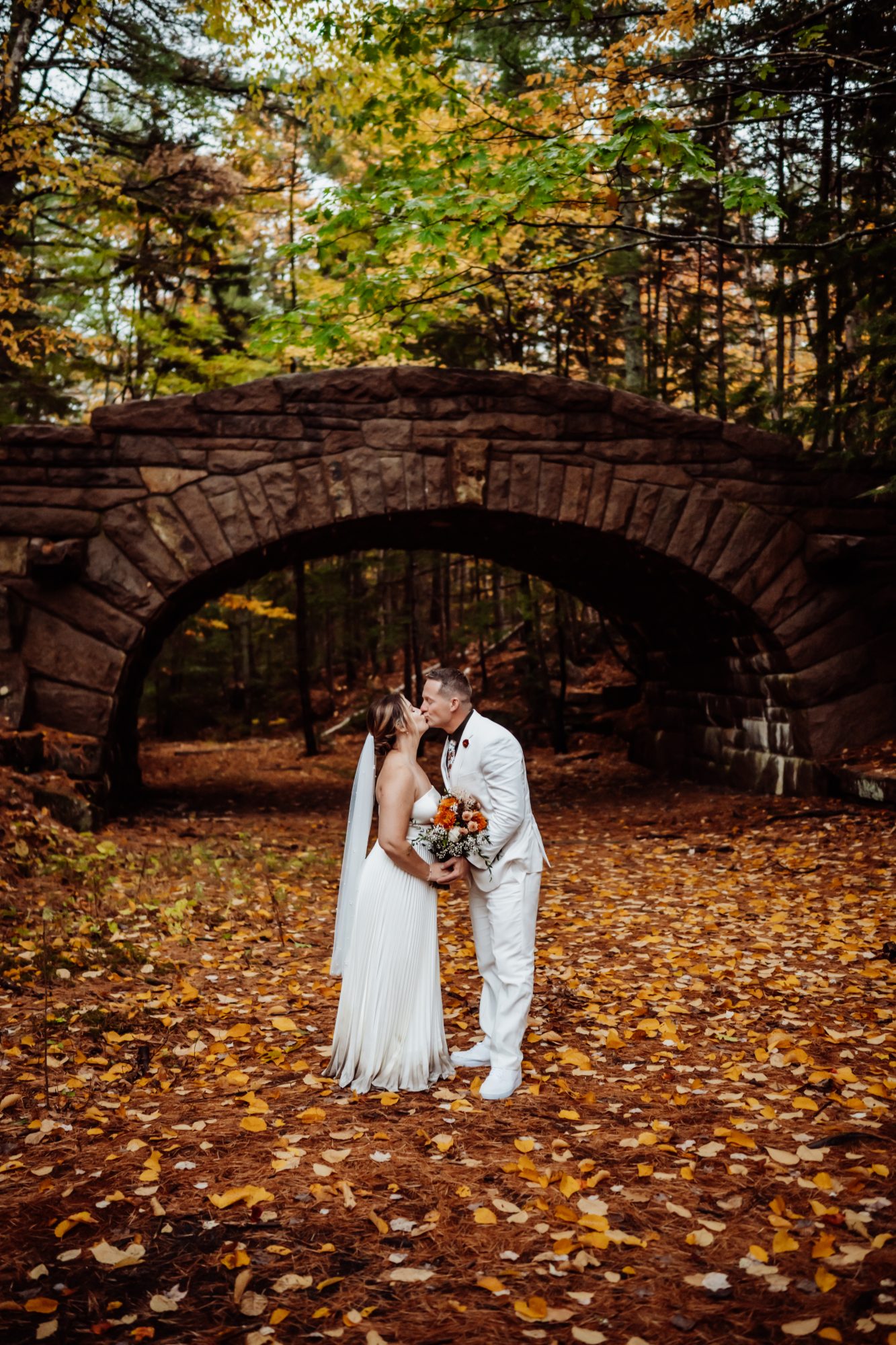 Bride and groom under stone bridge in Acadia National Park during fall elopement.