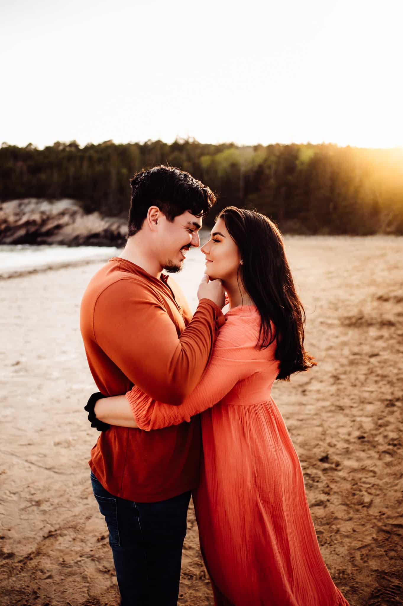 Brunette woman wearing orange dress with fiancé on sand beach