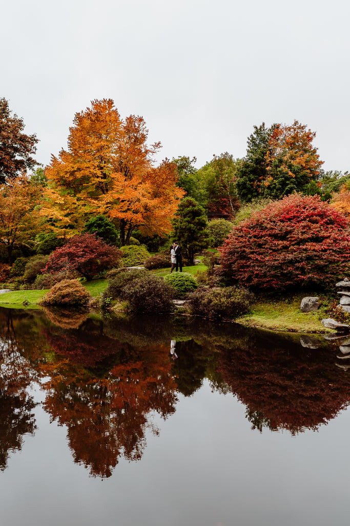 Couple standing on lawn among the reflective water at Asticou Azalea Garden