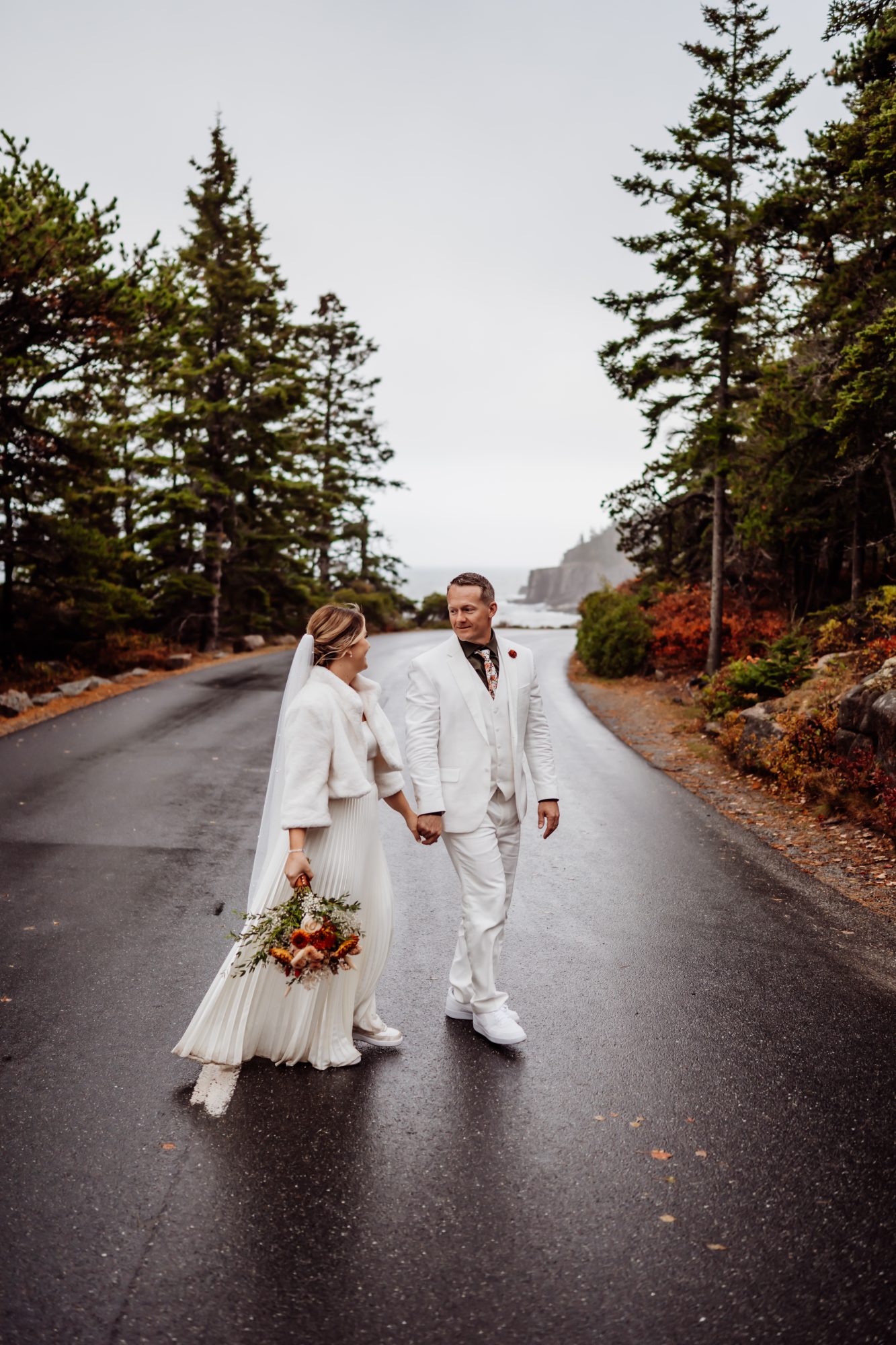 Newly married couple walking hand in hand along scenic road in Acadia.